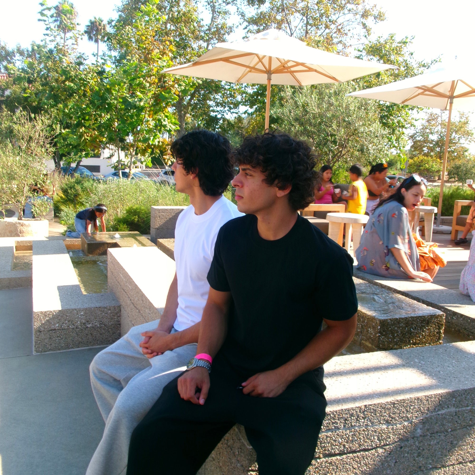 Two models wearing black and white SJ Goods shirts in an outdoor courtyard