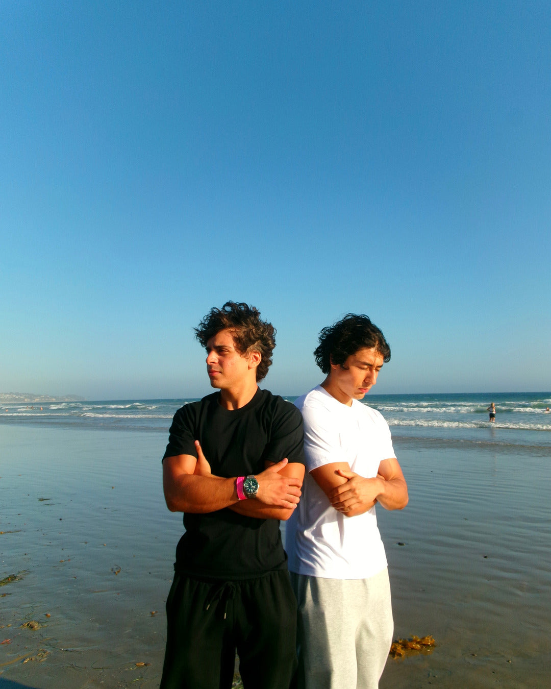 Two models in black and white SJ Goods shirts standing on a beach