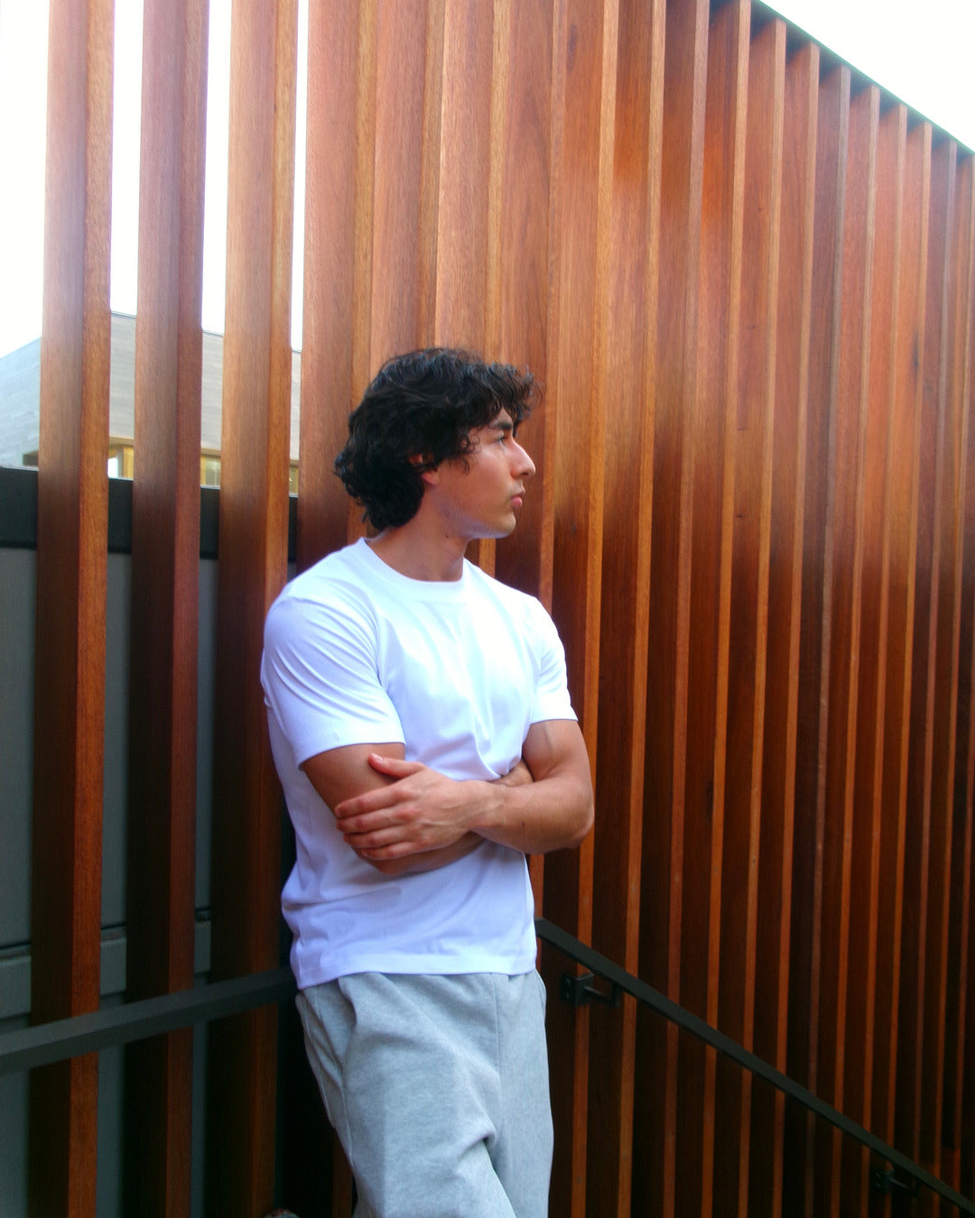 Model in a white SJ Goods shirt beside a warm wood screen